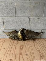 Front view of the vintage heavy brass American eagle wall hanging showing detailed feathers, shield, and objects in talons.