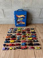 Blue Hot Wheels 48-Car Carry Case and 48 Hot Wheels cars arranged on wooden surface in rows.
