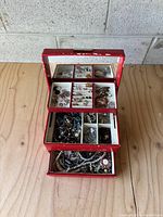 Red jewellery box standing open showing three levels of compartments and mix of costume jewellery inside