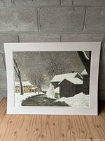 Full view of the framed winter landscape print depicting snow-covered houses, trees and a stream.