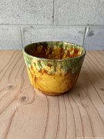 Front angle view of the pottery planter showing the glossy drop-glaze finish with green and amber hues on a yellow base.