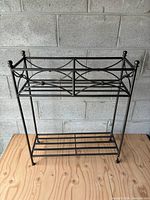 Full view of metal plant stand showing geometric design and two-tier shelving surface.