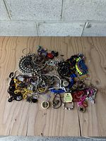 Image showing a large mixed lot of assorted costume jewellery laid on a wooden surface, featuring multiple necklaces, bracelets, pendants, and earrings in various colors and styles.