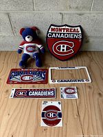 All items in the lot displayed on wooden surface against concrete wall including teddy bear, license plate cover, novelty plate, and stickers