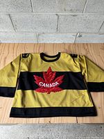 Full front view of yellow and black striped hockey jersey with central red maple leaf and Canada text.