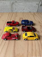 Front view of six pullback toy cars arranged on a wooden surface in two rows, showing colors and styles.