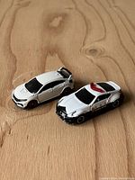 Two white and black Tomica toy cars displayed side by side on a wooden surface. Left is Honda Civic Type R, right is Nissan Fairlady Z Nismo police car.