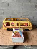 Yellow 1976 Barbie Star Traveler Camper shown with Barbie fashion doll carry trunk in front, displaying side view and scale.