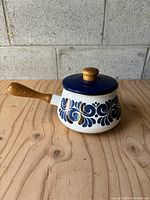Side view showing the fondue pot with blue and white Dutch pattern, wooden handle, and lid with knob.
