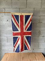 Full front view of the vintage Union Jack flag mounted on a wooden pole, showing overall wear and fabric condition.