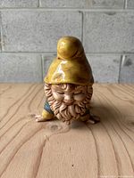 Front view of vintage ceramic garden gnome with detailed face and yellow hat, showing wear.