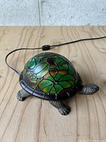 Turtle shaped lamp with dark green stained glass shell featuring frog patterns, power cord visible