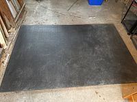 Top view of large black exercise mat laid on concrete floor showing full size and surface condition