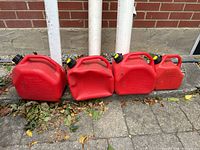 Four red plastic gasoline cans of varying sizes lined up on a stone surface with a brick wall background