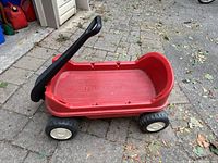 Full view of Fisher Price red wagon showing overall shape, black handle, and wheels on outdoor surface with some fallen leaves.