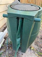 Photo of green rain barrel showing the hose connection area with dented spout and 'Made in Canada' marking.