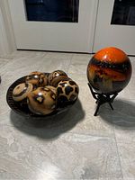 Photo showing six decorative animal print balls inside a zebra striped bowl and the large painted lion ball on wooden stand in background.