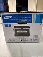 Box front showing Samsung branding, monochrome laser multifunction capabilities, and device image highlighting one-touch screen print, eco print, and compact size.