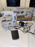 Dressmaker II Sewing Center box, sewing machine, foot pedal and power adapter all shown together on a table.