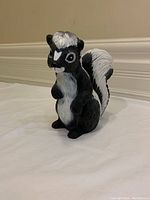 Front view of a black and white skunk lawn ornament, standing upright with detailed fur texture and facial features, approximately 7.5 inches tall.