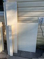 Multiple solid painted wood planks leaning against an exterior wall under natural daylight, showing sizes and paint condition.