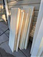 View of solid white painted wood planks leaning against siding outside. Shows length and width of planks.