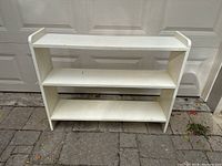 Full front view of white painted three-shelf solid wood shelf showing overall structure and surface condition.