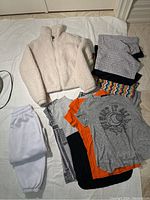 Overview of lot including white zippered fluffy sweater, white sweatpants, four folded T-shirts, and three bike shorts underneath