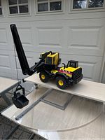 Front side view of the Tonka Mighty 758 crane, showing the extended black boom with bucket, yellow operator cab, large yellow wheels and Tonka logo details.