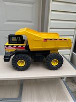 Side profile photo showing the full length yellow metal dump bed, black cab, and large rubber tires