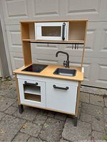 Front view of the wooden toy kitchen showing microwave, stovetop, sink, cabinet, and oven door.