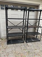 Two black metal shelving units standing side by side in front of a garage door, showing overall structure and condition.