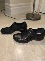 Pair of black leather Merrell women's slip-on shoes displayed side by side on floor showing outer and side profile