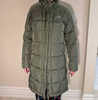 Front full view of olive green women's Northface winter coat below knee length on model with sleeves long and closed zipper