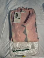 Folded pink, grey, and white Lyle & Scott lambswool sweater with original tag attached and transparent plastic packaging underneath on white fabric surface.