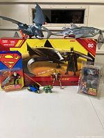 Wide view of all items including large Batwing toy in box, small figures, and two packaged figures.