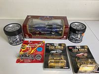 Photo of six items: boxed blue Shelby Cobra die cast model car, two 24K gold plated NASCAR collectible cars in sealed packaging, Johnny Lightning Hot Wheels car sealed in blister pack, and two Harley Davidson cylindrical collectible containers with motorcycle figures.