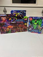 Three boxed He-Man and the Masters of the Universe items on a white table: Skeletor figure on Talon Fighter vehicle, green Skeletor figure in another box, and a playset box below.