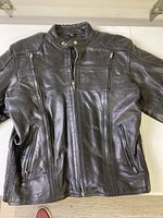 Front view of black leather motorcycle jacket showing full length zipper, two zipped chest pockets, and two zipped side pockets.