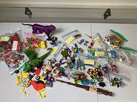 Wide photo showing multiple loose toys spread on a flat surface including plastic animal figures, small vehicles, and multiple zip bags containing smaller toys.