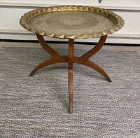 Front view of the round Moroccan style side table with brass top on wooden foldable legs sitting on a grey carpet.