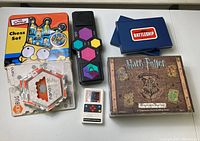 Overview of all items on a white surface showing Simpsons Chess Set, Harry Potter game box, electronic basketball game, Hexbug Nano packaging, Battleship card decks, and Simon style electronic game