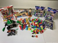 Multiple toys on a white surface showing boxed Akedo sets, PEZ dispensers, Crazy Bones figures, and a bobblehead figure