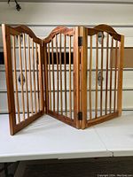 Full view of the three-panel wooden pet gate standing on a white surface showing the gate's overall structure and size.