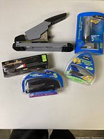 All 5 staplers laid on a white table showing packaging and one loose gray and black stapler