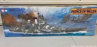 Box front showing painted depiction of the British battleship Prince of Wales at sea with smoke and two other ships in background. Tamiya branding in upper left corner.