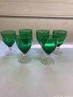 Set of six vintage green glass goblets with bubble footed bases arranged on a white surface.