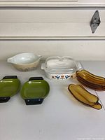 All items of vintage glass and ceramic cookware arranged on table: Corning Ware casserole, Corelle mixing bowl, green pans, amber oval dishes