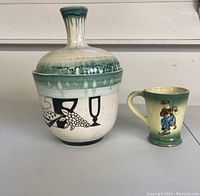 Photo of two items: a green Dutch mug and a ceramic studio-style vase with black wine imagery