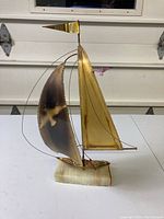 Side angle view showing brass sailboat sculpture with flying seagull motif and quartz base on white background.